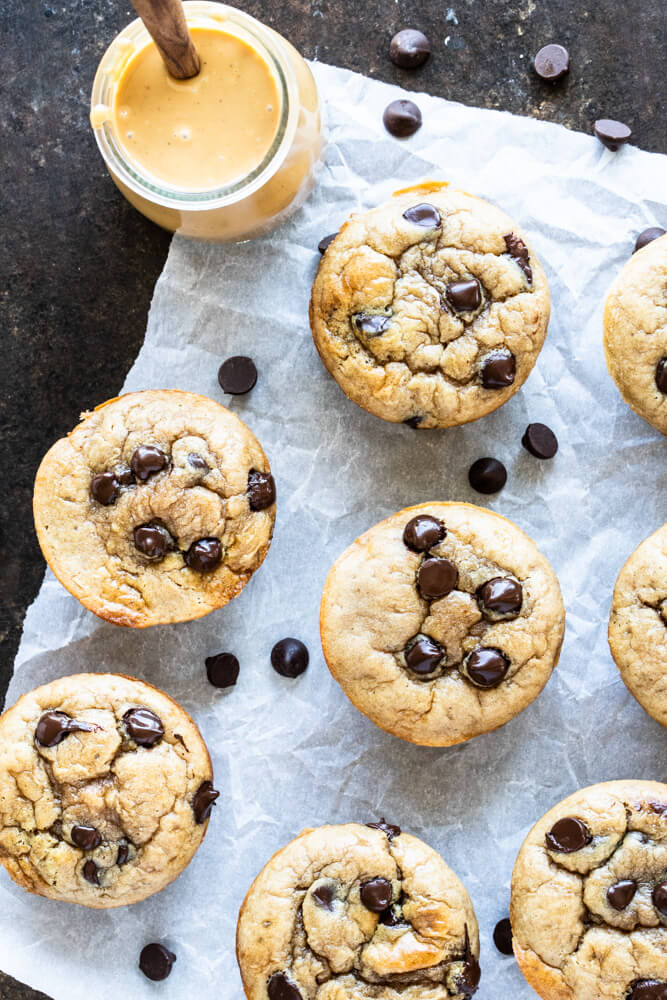 peanut butter chocolate chip muffins on white parchment paper and a jar of peanut butter