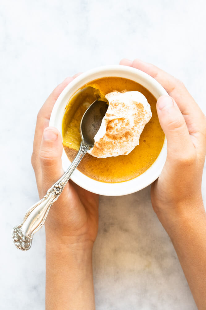 hands holding small bowl of pumpkin custard