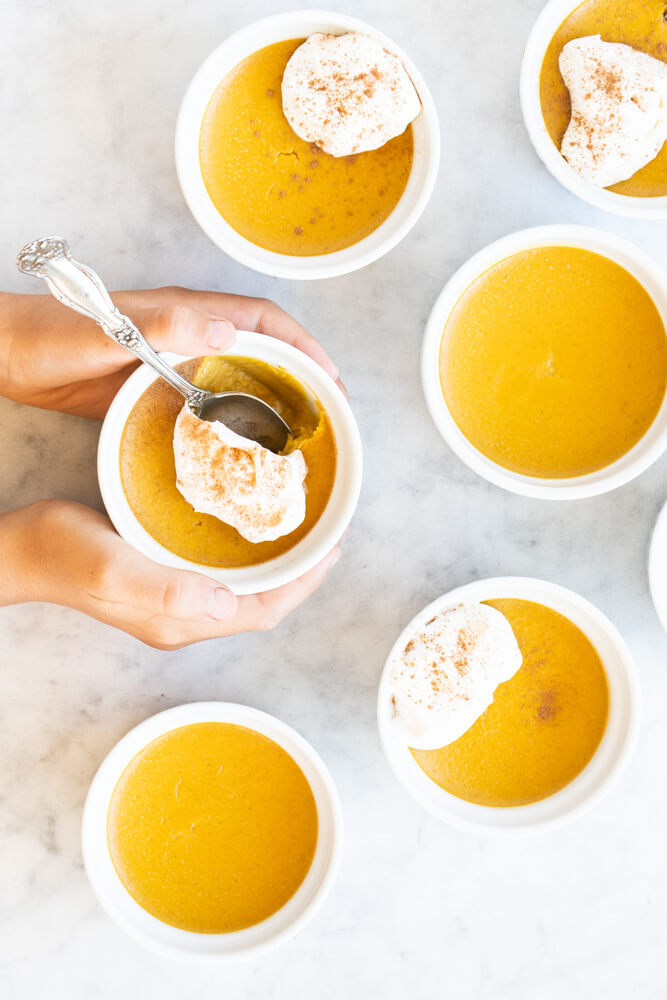 hands holding white bowl with pumpkin custard with a spoon in it