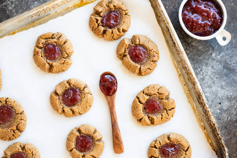 peanut butter and jelly thumbprints on cookie sheet with a wooden spoon