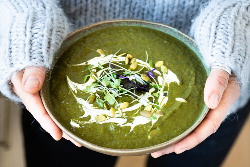 two hands holding detox green soup in green bowl
