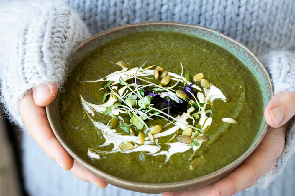 hands holding green bowl with detox green soup
