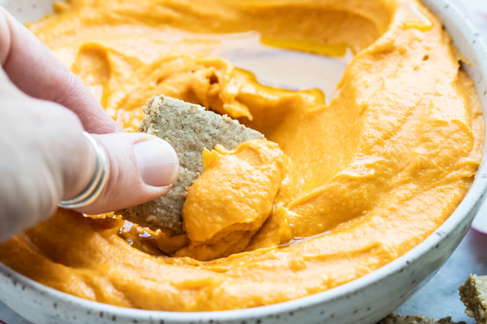 hand dipping cracker in sweet potato hummus