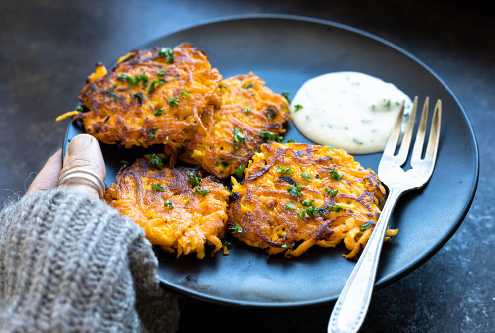 hand holding black plate with butternut squash fritters