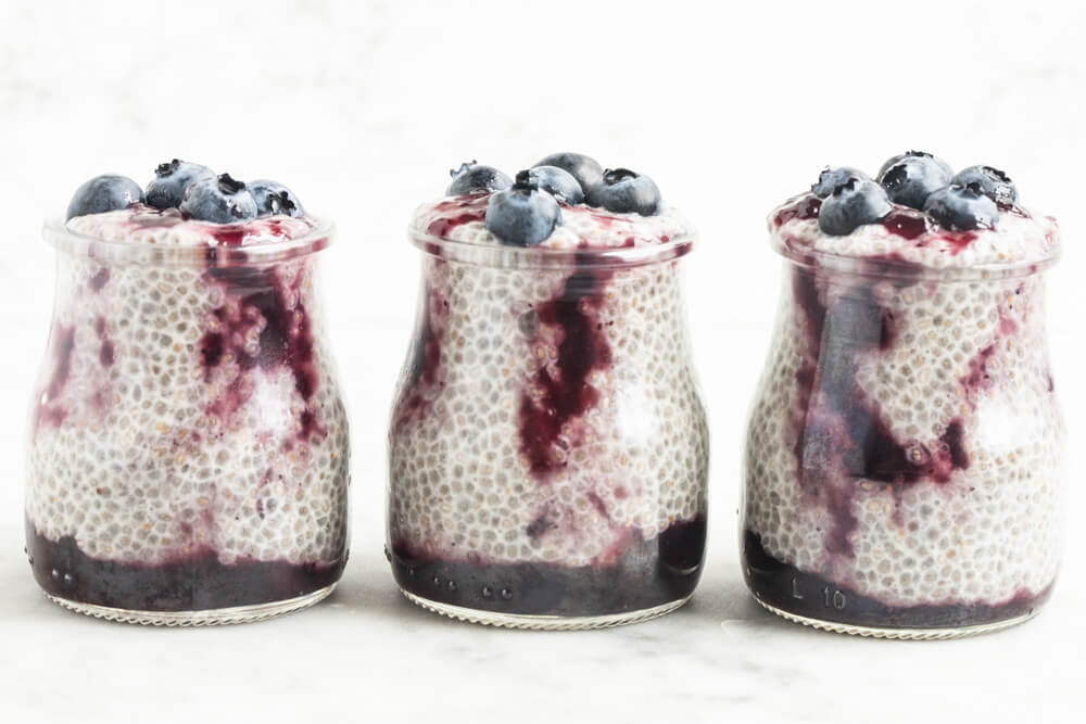 three jars of blueberry jam chia pudding on white table