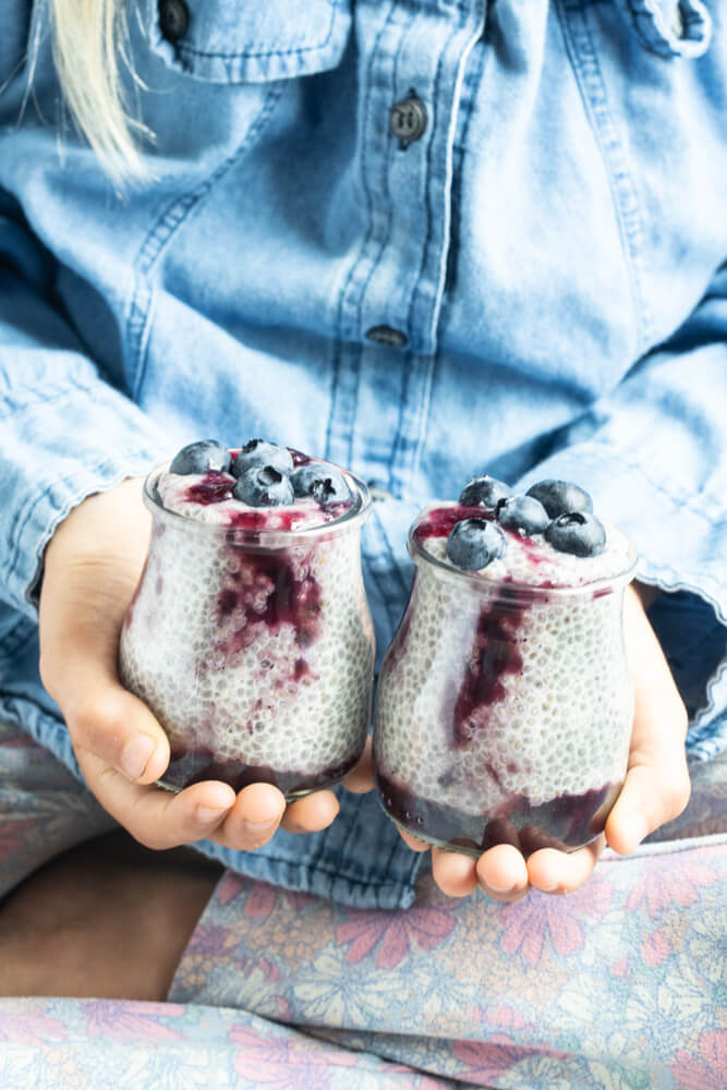 two hands holding jars of blueberry chia pudding