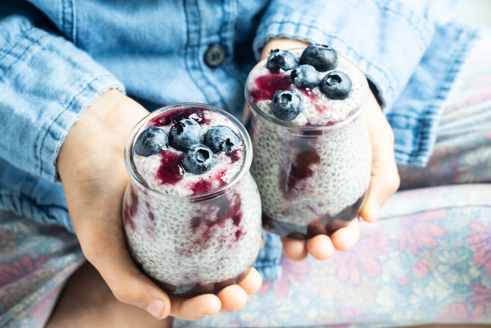 child holding two jars of blueberry jam chia pudding