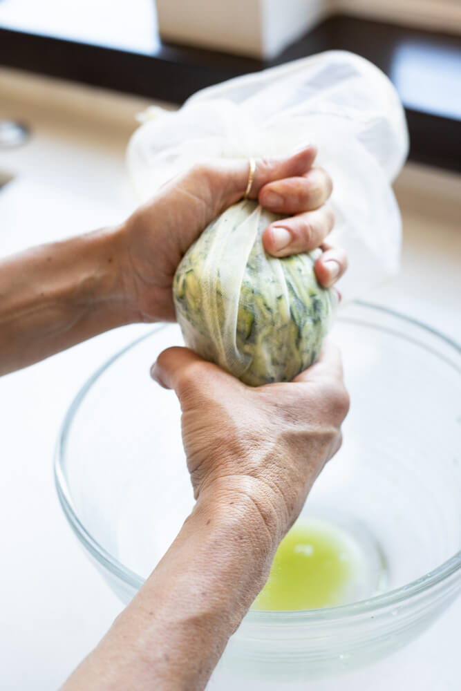 hand squeezing zucchini in nut milk bag