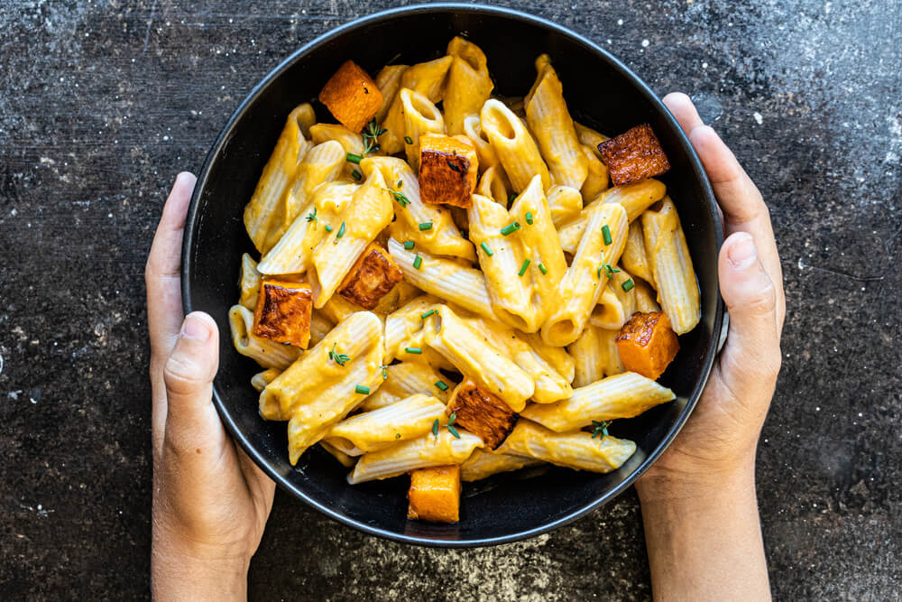 hands holding black bowl of pasta