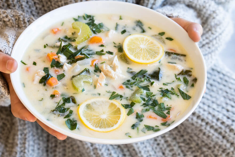 white bowl of chicken soup held in hands