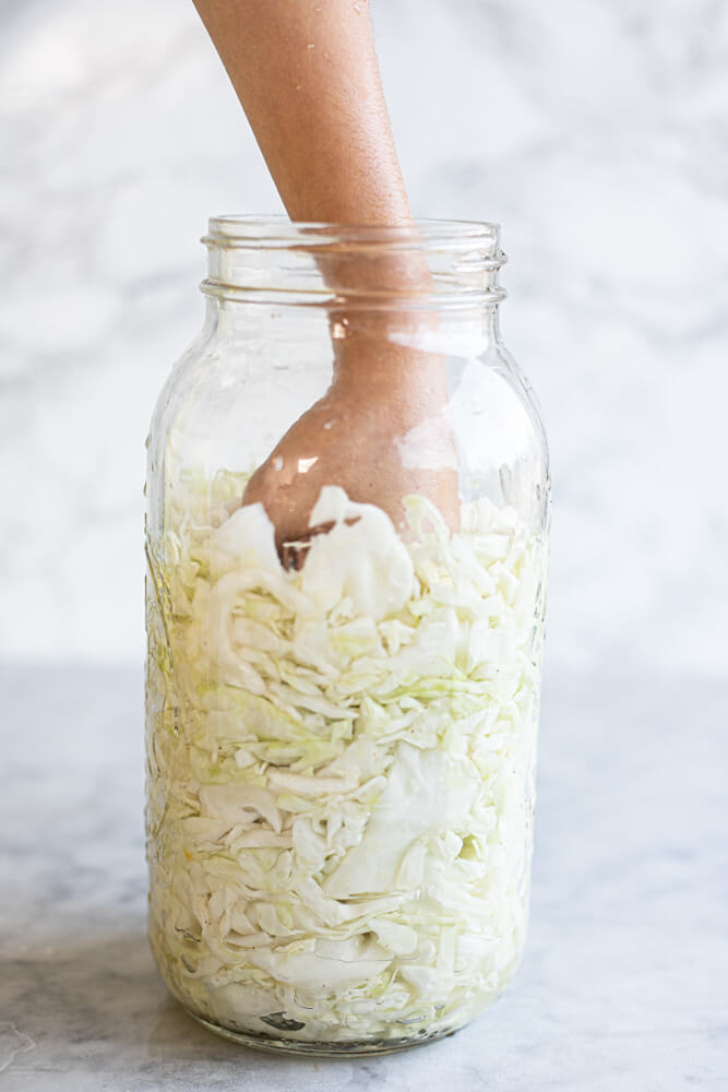 hand pressing cabbage in large glass jar
