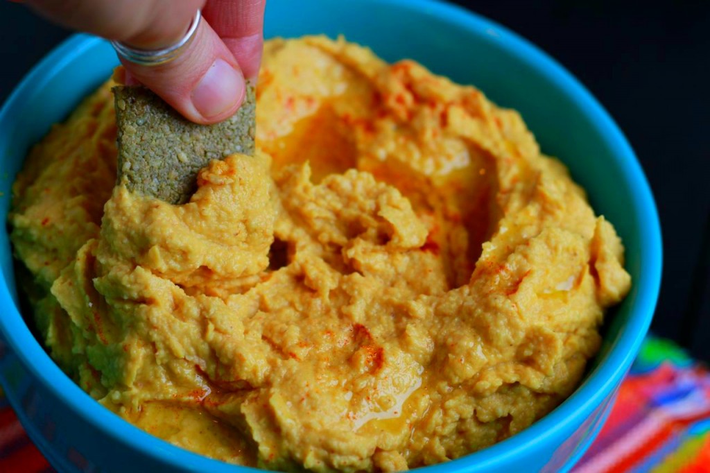 hand dipping a chip into hummus in blue bowl